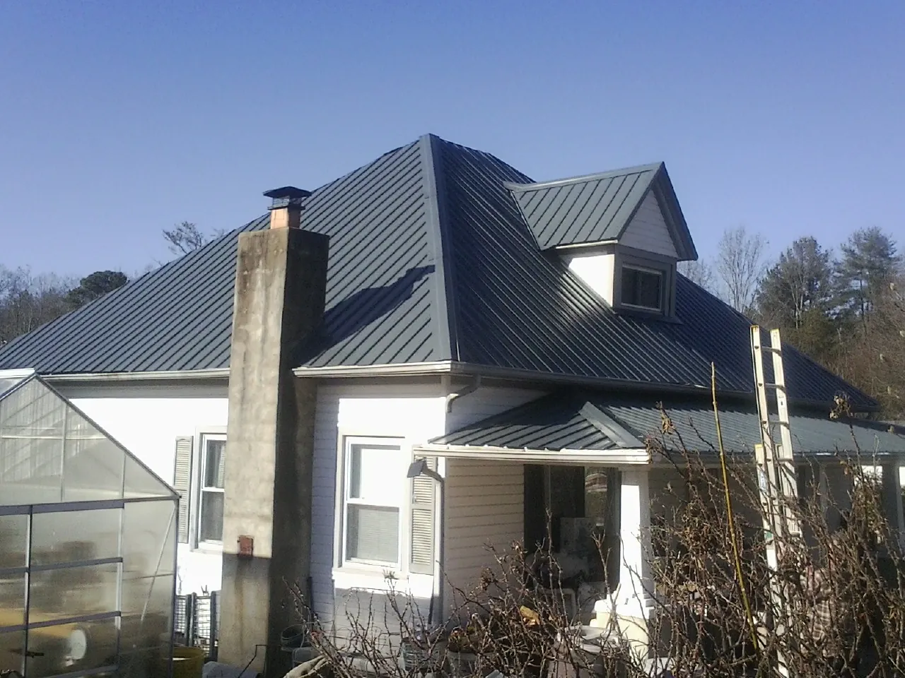 Dark blue standing seam metal roof on a white farmhouse with dormer — Slate & Tile Roof Repair by Roofing Brothers in Centennial