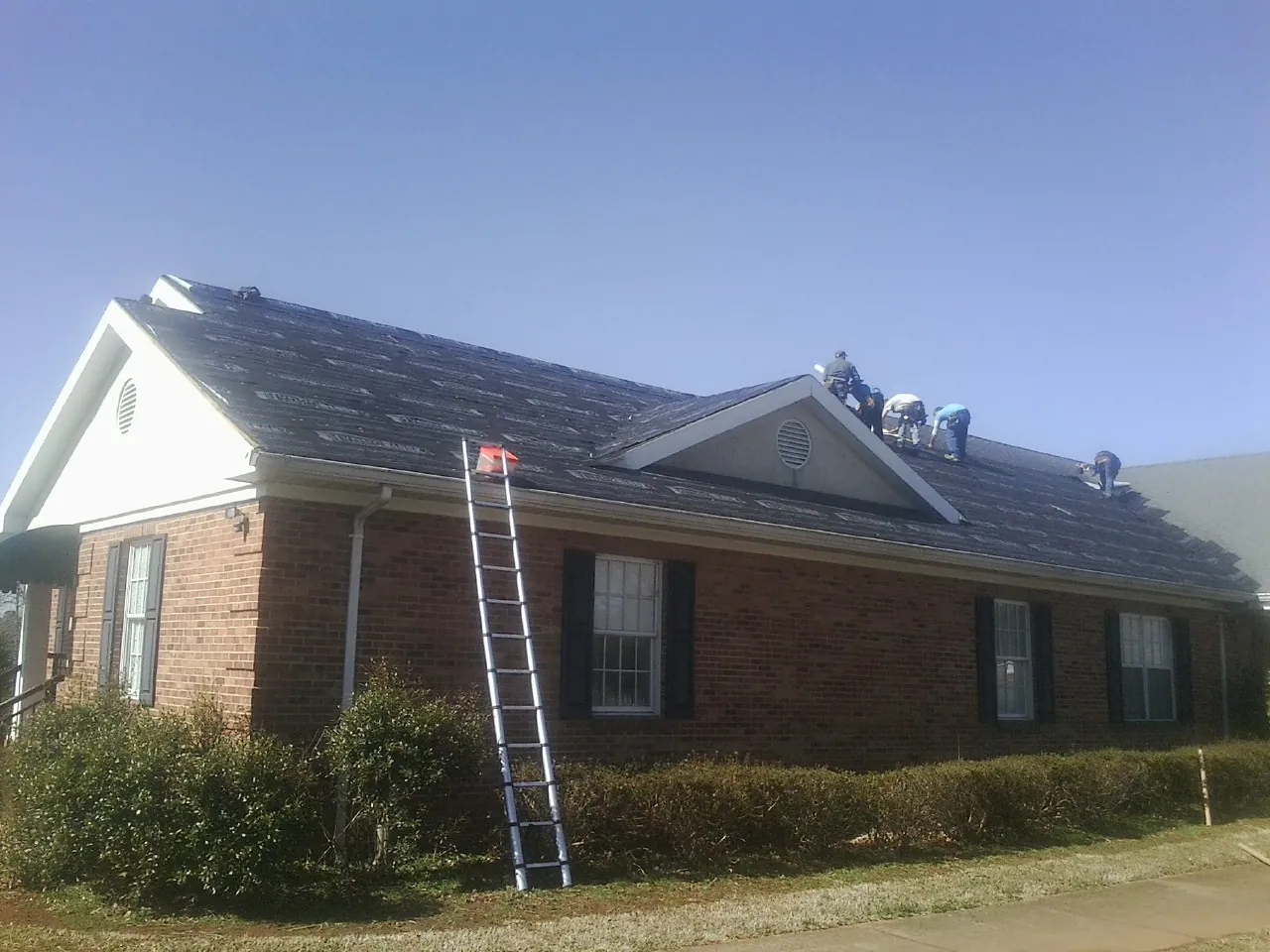 Crew tearing shingles off a brick ranch roof with a ladder set — Metal Roof Repair work by our crew in Centennial