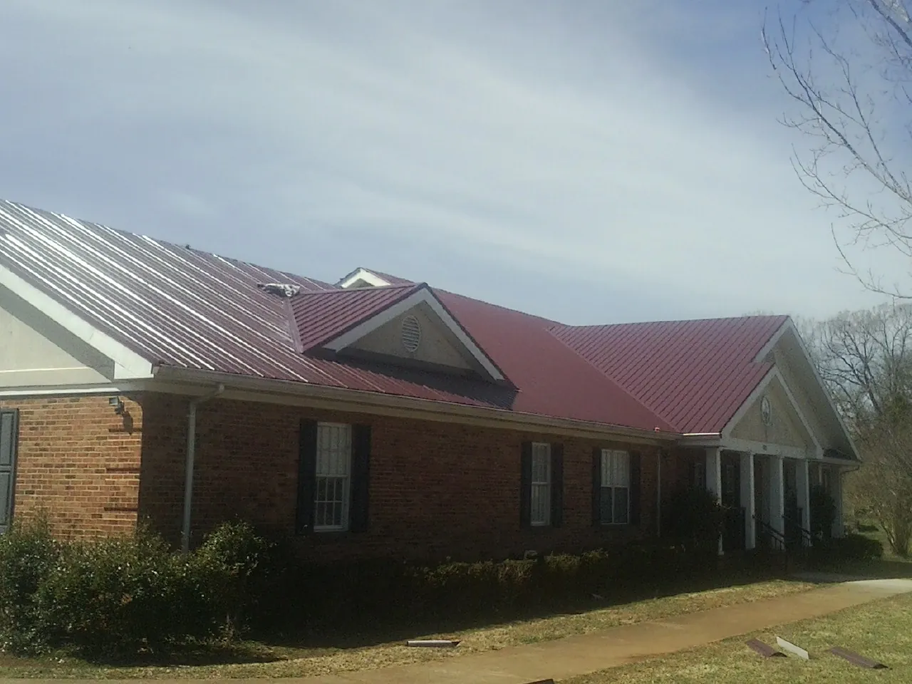 Red metal roof with gabled entries on a long brick building, from a Hail Damage Roof Repair job in Centennial