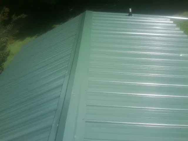 New green metal panels meeting at the ridge of a roof — Flat Roof Repair work by our crew in Centennial