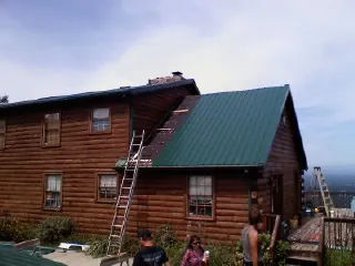 Green metal roof going on a two story log home with ladders set in Centennial