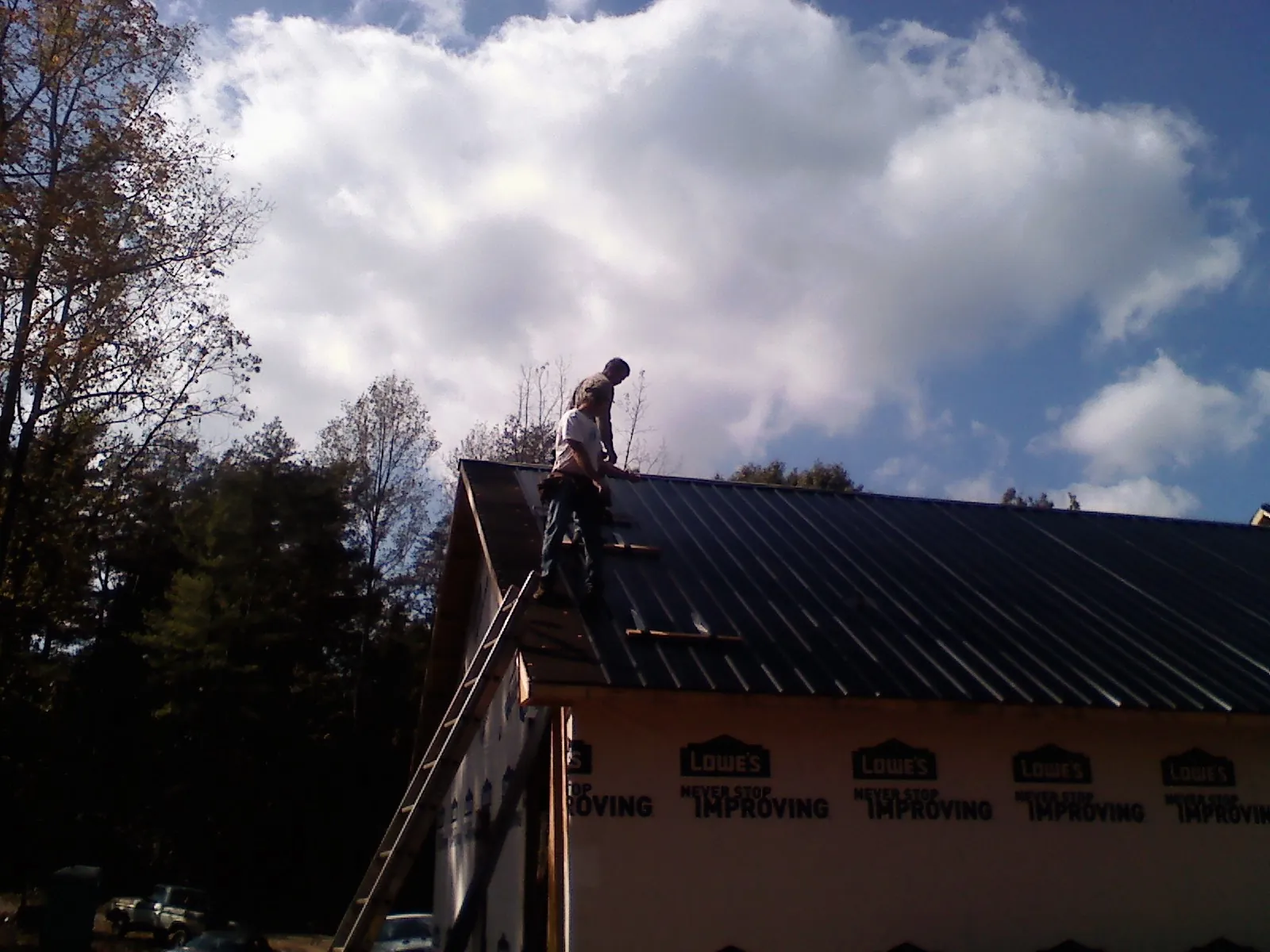 Roofer fastening dark metal panels high against a cloudy sky, from a Roof Inspection job in Centennial