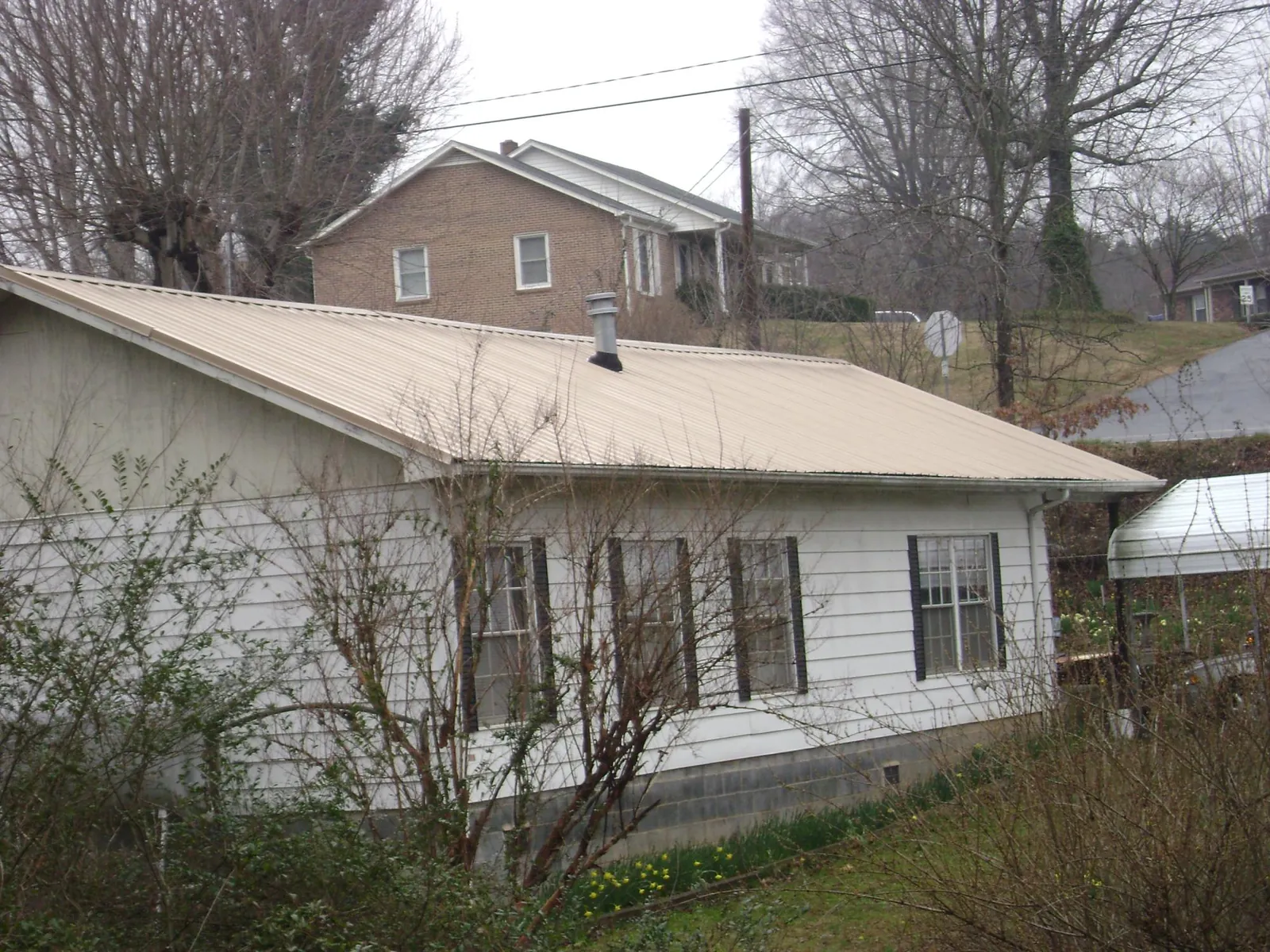 Tan metal roof on a white sided house set into a hillside — Commercial Roofing by Roofing Brothers in Centennial